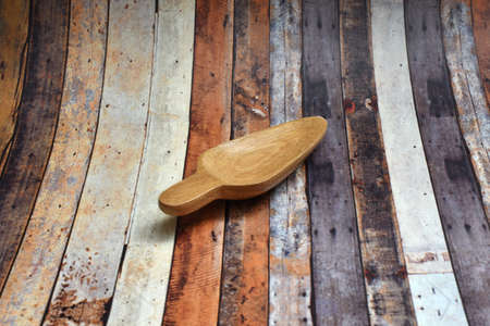 A small brown spoon made of wood with a real wood motif against a wooden plank ornamentの写真素材
