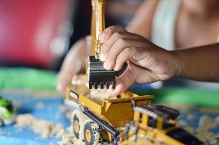 toddlers are playing sand trucks and yellow excavators with hands holding children's sand toys