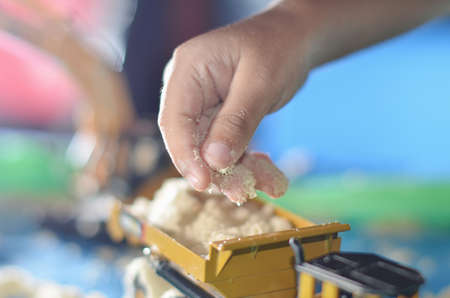 toddlers are playing sand trucks and yellow excavators with hands holding children's sand toys