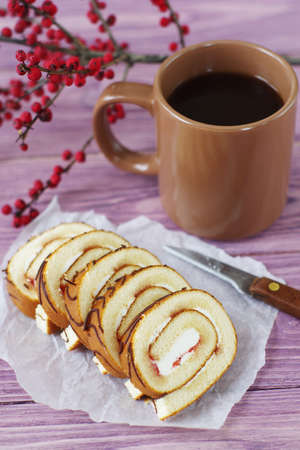 Sliced ??swiss roll with jam on a wooden pink background. Dessert and a cup of hot coffee.の写真素材