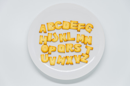 Alphabet shape cracker on dish with white backgroundの写真素材