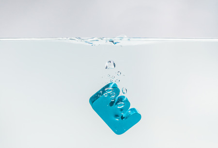 Blue wooden alphabet E drop in the water with white background and selective focusの写真素材