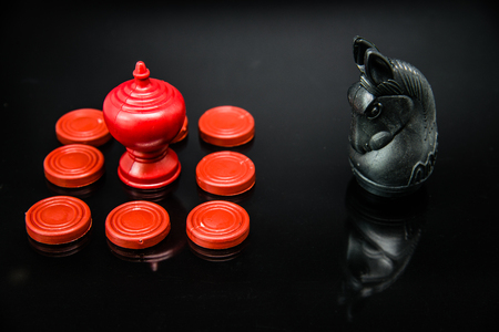Red King chess in group of pawns challenge with Black Knight Thai chess piece on black background...