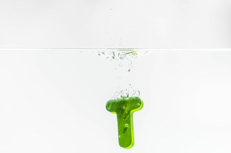 Green wooden alphabet T drop in the water with white background and selective focusの写真素材