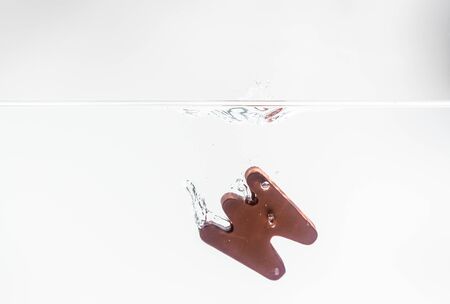 Brown wooden alphabet W drop in the water with white background and selective focus