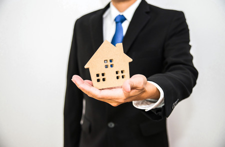 Business man hold wooden house toy on hand with isolated white backgroundの写真素材