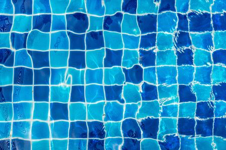 Blue ceramic floor in swimming pool with ripple wave water and sun reflection in background conceptの写真素材
