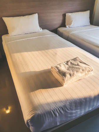 Clean white towel on white clean bedroom in the budget hotel for traveller with sunset light from...