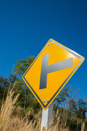 Yellow Cross section traffic sign in the countryside with dried grass and blue sky for travel concept ideaの写真素材