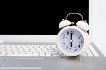 Alarm clock and portable computer put on the desk, with white background.の写真素材