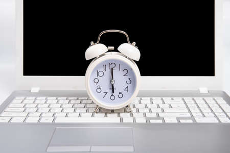 Alarm clock and portable computer put on the desk, with white background.の写真素材