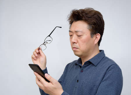 Asian male trying to read something on his mobile phone. poor sight, presbyopia, myopia.の素材 [FY310134931279]