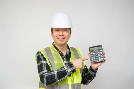 A middle-aged Asian man wearing a white work cap and work suit holding a calculator in his hand.の写真素材