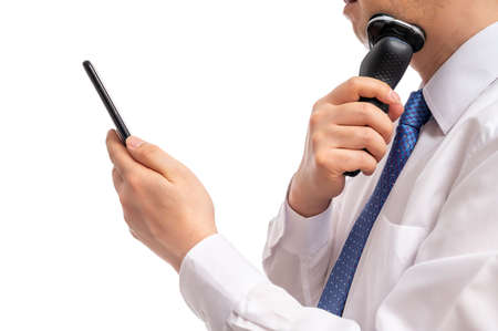A businessman looking at a smartphone while shaving. Morning rush hour.の写真素材