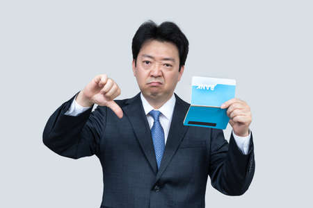 A middle-aged Asian businessman holding a bank passbook in his hand on a gray background.の写真素材