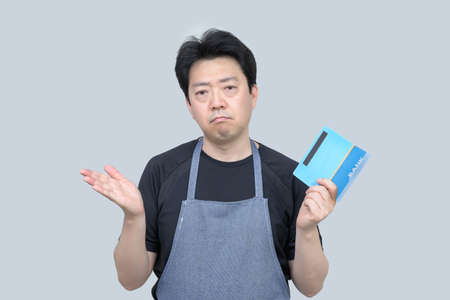 A middle-aged Asian man holding a bank passbook in his hand on a gray background.の写真素材