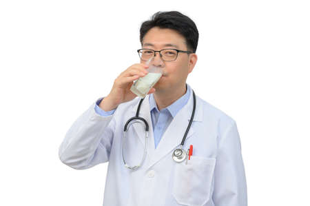 A middle-aged Asian doctor is drinking a glass of fresh milk on a white background.の写真素材