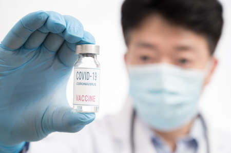 The doctor's hand wearing blue gloves against white background and holding Covid-19 vaccine.の写真素材