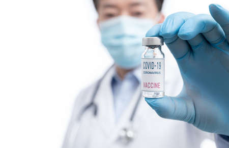 The doctor's hand wearing blue gloves against white background and holding Covid-19 vaccine.の写真素材