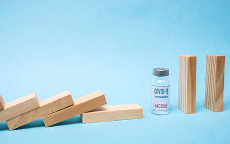 Vaccine concept with wood domino and COVID-19 vaccine ampoule on blue background.の写真素材