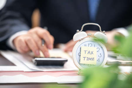 Alarm clock with tax time note and Businessmen using calculators.の写真素材