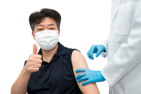 A gloved doctor holding a syringe gives a vaccine injection to an Asian middle-aged male patient wearing a medical mask.の写真素材
