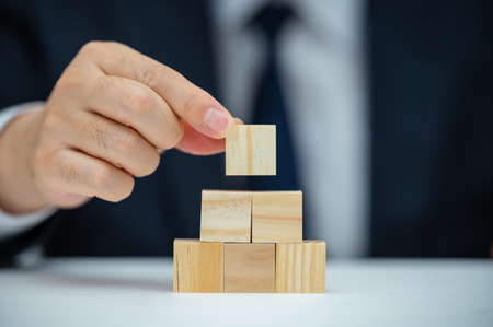 The hands of a male businessman who is stacking wooden blocks. Business concept.の写真素材
