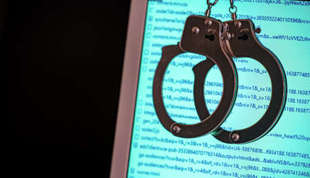 Blurred computer screen with program code visible, and shaking handcuffs. Cybercrime conceptの写真素材