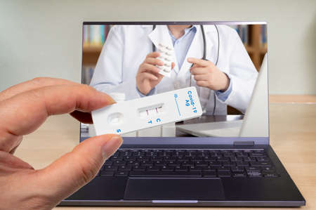 A male hand holding a COVID-19 rapid antigen test kit with two red lines indicating positive.の写真素材