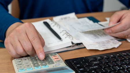 A man is writing a household ledger while organizing receipts. A close-up of hands. Tax or year-end settlement concept.の写真素材