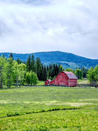 A bright red barn stands in a lush green field by trees near Twin Lakes, Idaho.