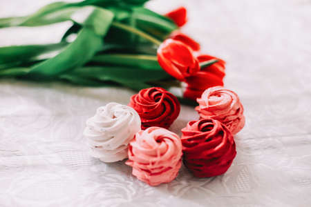Red and white zephyr with red tulips on white table. Marshmallows and a bunch of tulipsの写真素材