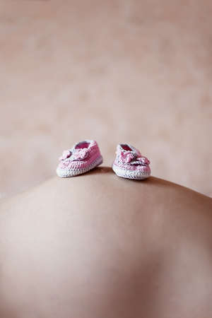 Pregnant belly with pink baby booties and pink backgroundの写真素材