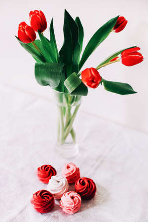 Red and white zephyr with red tulips on white background. Marshmallows and a bunch of tulipsの写真素材