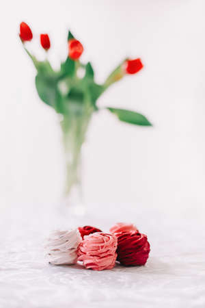 Red and white zephyr with red tulips on white background. Marshmallows and a bunch of tulipsの写真素材