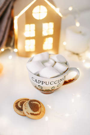 A cup of christmas hot coffee with marshmallow on the background of New Year's lights and decorationsの写真素材