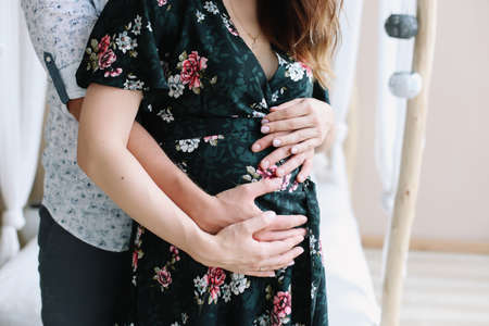 Close up of parents hands touching pregnant belly at home. Pregnancy, maternity, preparation and expectation concept.  Beautiful tender mood photo of pregnancy.の写真素材