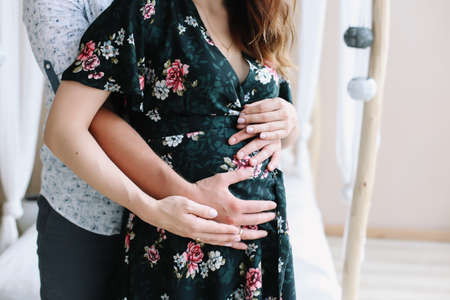 Close up of parents hands touching pregnant belly at home. Pregnancy, maternity, preparation and expectation concept.  Beautiful tender mood photo of pregnancy.の写真素材