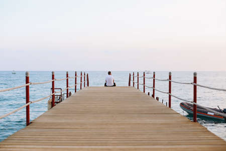 Man sitting on the pier and looking at the sea horizon and blue sky. Vacation concept. Summer time sea vacation backgroundの写真素材