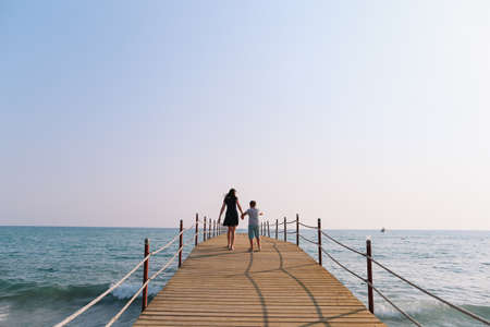 Mom and son walking along the pier. Sea horizon and blue sky. Family vacation at sea. Summer time sea vacation backgroundの写真素材