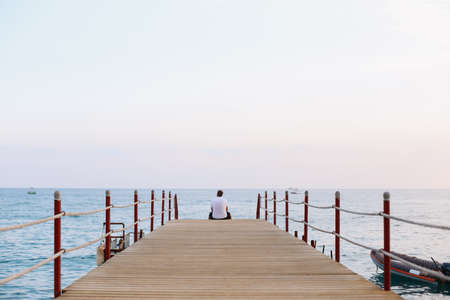 Man sitting on the pier and looking at the sea horizon and blue sky. Vacation concept. Summer time sea vacation backgroundの写真素材