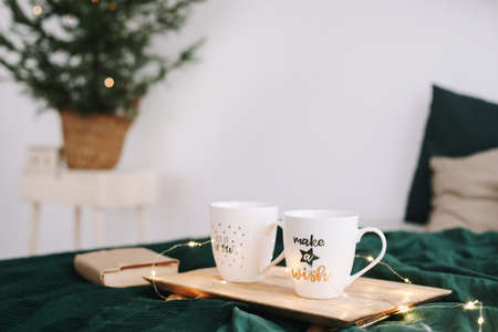 Cozy bedroom with coffee mugs and book in bed. Christmas still life. Breakfast in bed. Flat lay. Holidays, Christmas and winter conceptの写真素材