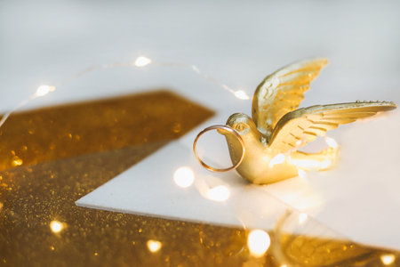Golden wedding rings on golden background with toy bird and decorations. Shiny golden jewelry. Wedding details. Proposal of marriage, valentine gift. copy space.の写真素材