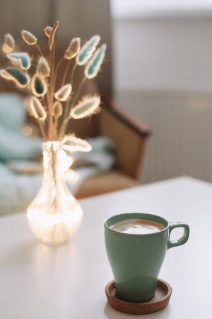 Cup of coffee and a transparent vase with dried flowers at white background