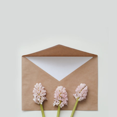 Craft paper envelop with white card and pink hyacinth flowers on white background. Top view, flat lay, copy space. Holiday festive minimal background.の写真素材