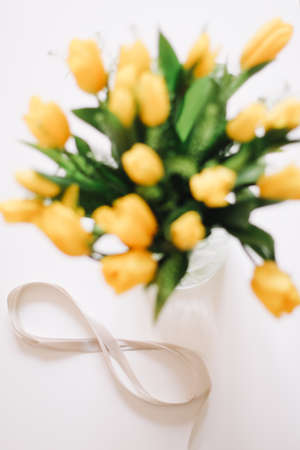 Figure eight of beige ribbon with beautiful yellow tulips in a vase. International Women Day, 8 March concept. Flowers illuminating yellow color of the year 2021