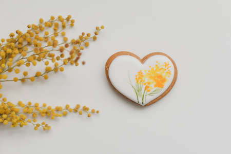 gingerbread cookie in a shape of a heart and mimosa flowers on white background. top view copy spaceの写真素材