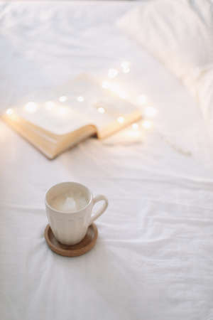Reading and having breakfast in bed. Coffee cup and a book in bed. Cozy sunny morning at home.の写真素材