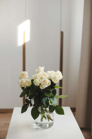 glass vase with white roses on white table indoorsの写真素材