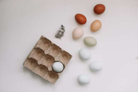 fresh chicken eggs of natural shades and colors in a recycled box on a white background